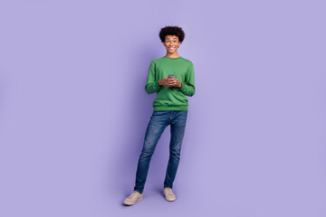 Fototapeta na wymiar Full length photo of funky cheerful guy wear green pullover texting messages modern device isolated purple color background