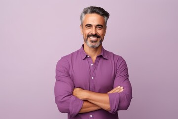 Portrait of handsome mature man with crossed arms looking at camera and smiling, standing against purple background