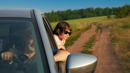 A car ride with a child. A little girl wearing sunglasses looks out the side rear window. In the...