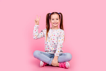Full size photo of pleasant schoolgirl dressed dotted pullover sit on floor showing v-sign symbol...