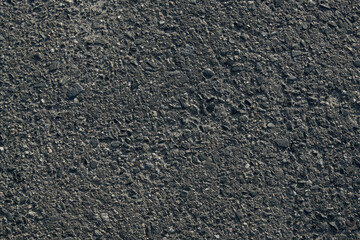 Close-up view captures texture of dark asphalt road. Small stones embedded in surface highlight rough, consistent material