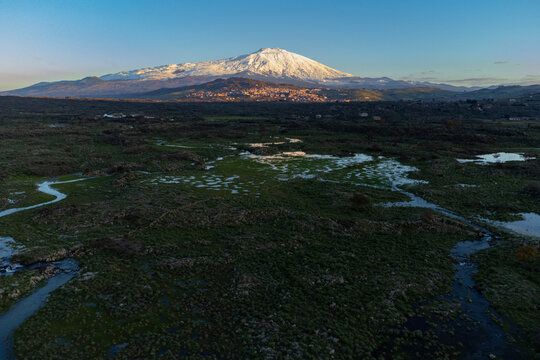 Bronte town under the snowy and majestic volcano Etna and a cloudy blue sky