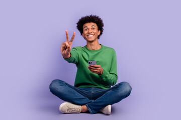 Full length photo of cute funky man dressed green sweater showing v-sign texting apple iphone...
