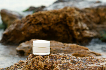 White glass jar of face cream on wet stone on sea water background. Mockup for your design. Beauty...
