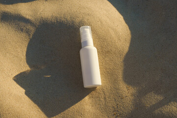 White mockup of a jar of face cream or serum with a dispenser on sea sand illuminated by sunset light. Concept of natural cosmetics and organic beauty products