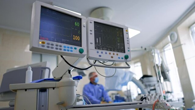 Monitoring condition of a patient under operation. Screens of lung ventilating machine displaying life signs. Low angle view.
