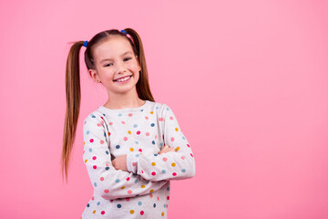 Portrait of optimistic adorable schoolgirl with ponytails dressed dotted sleepwear holding palms folded isolated on pink color background