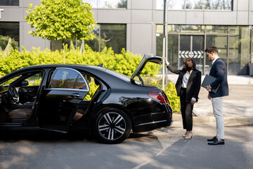 Female chauffeur opens a car trunk, handsome businessman going to use luxury taxi service during a business trip. Concept of business transfer services, idea of personal driver.