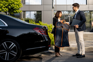 Female chauffeur gives a businessman his suit, after a business trip in luxury taxi. Concept of...