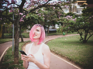 Woman with pink hair in the park with a cell phone