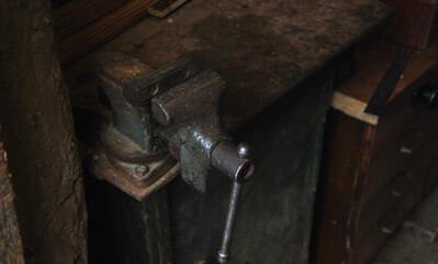old bench vise on the workplace in an old workshop. dark vintage photo.