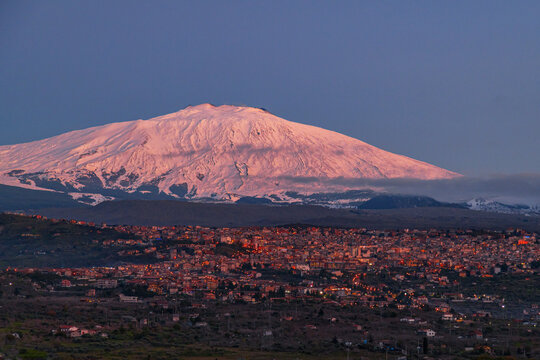Bronte town under the snowy and majestic volcano Etna and a cloudy blue sky