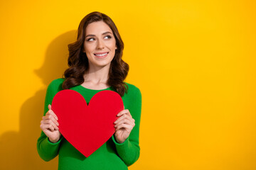 Photo of lovely cute woman dressed green stylish clothes hands hold red paper card look up empty space isolated on yellow color background