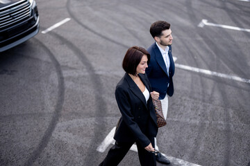 Business couple walking on parking lot, arrived by luxury SUV taxi, view from above. Concept of...