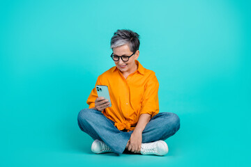 Full body size photo of focused working business woman pensioner browsing smartphone sit floor isolated on aquamarine color background