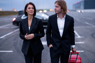 Business couple walking with a suitcase on parking lot, arrived by luxury taxi. Concept of...