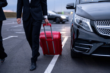 Business couple walking with a suitcase on parking lot, arrived by luxury taxi. Cropeed view with...