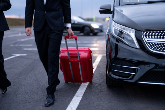 Business couple walking with a suitcase on parking lot, arrived by luxury taxi. Cropeed view with no face. Concept of transportation and business trips