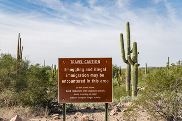 Sign near US - Mexican border wall reading Caution smuggling and illegal immigration in this area -...