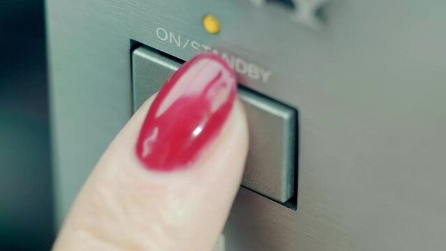 A female finger with a beautiful red nail, with a bright highlight, presses the power button on electrical equipment. Closeup. Macro. Shallow depth of field