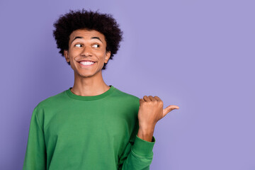 Photo of tricky excited guy wear green pullover pointing thumb looking empty space isolated purple...