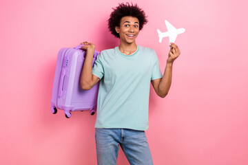 Photo of cheerful positive man dressed blue t-shirt holding luggage paper plane card isolated pink...