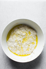 Focaccia dough in a white bowl, process of making focaccia, dough rising in a white mixing bowl