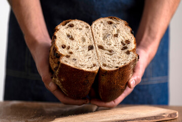 hands holding big homemade sourdough bread with seeds and cereals and bread knife cutting into...