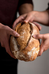 hands holding big homemade sourdough bread with seeds and cereals and bread knife cutting into slices