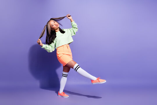 Full size photo of nice pleasant korean girl wear oversize pullover hold two hair tails dancing isolated on violet color background