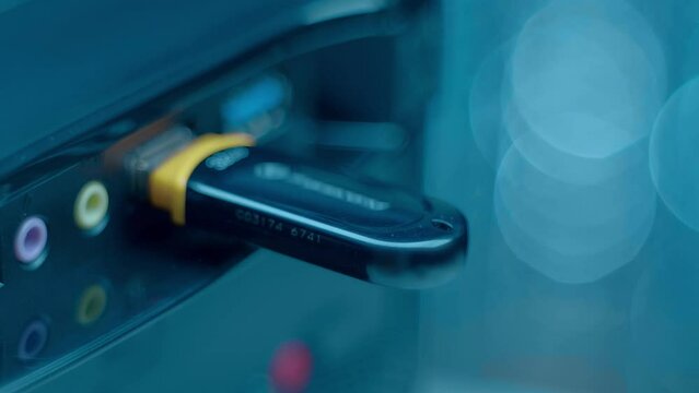 A man&rsquo;s hand inserts (remove) a black, shiny flash drive into the USB port of computer against a blurred background. Closeup. Macro. Shallow depth of field. Shot in motion