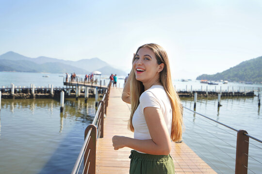 Happy beautiful young woman walking on pier Comodo Magalhaes on Ubatuba promenade, Costa Verde, Brazil