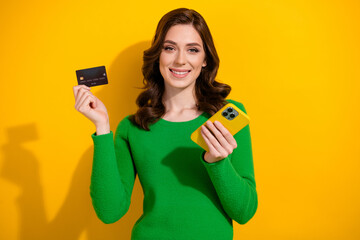 Portrait of lovely cheerful person toothy smile hold smart phone debit plastic card isolated on yellow color background