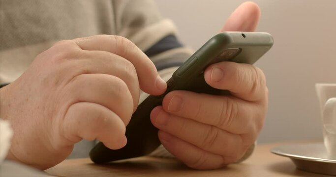 Senior man using contactless payment at a cafe through a mobile application. Modern method of payment involves utilizing mobile app on a smartphone to complete transactions. Seniors hands close-up.
