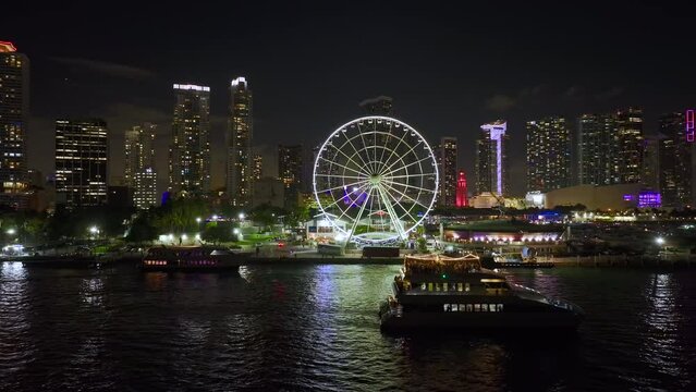 Miami Observation Wheel at Bayside Marketplace with reflections in Biscayne Bay and illuminated skyscrapers of Brickell, city's financial center. Urban landscape at night
