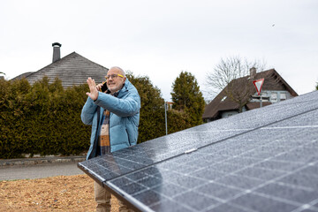 Smiling  senior businessman examining solar panel while talking by telephone 