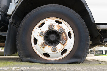 Flat truck tire on axel with rust on wheel hub with deflated tire on ground