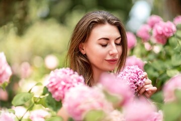 Fototapeta premium Hydrangeas Happy woman in pink dress amid hydrangeas. Large pink hydrangea caps surround woman. Sunny outdoor setting. Showcasing happy woman amid hydrangea bloom.