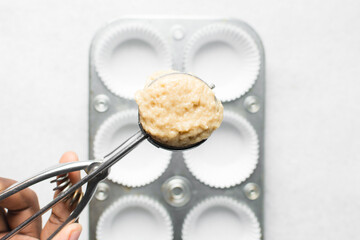 scooping vanilla almond muffins batter in a cupcake pan, top view of almond muffins batter, process of making almond muffins