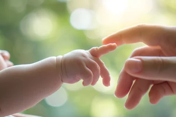 Fotobehang A close-up of a baby's tiny hand reaching to grab an adult's finger, symbolizing care and love. © Enigma