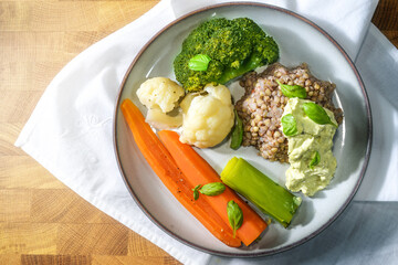 Vegetables with buckwheat, cream cheese dip and basil garnish on a plate, a white napkin and a rustic wooden table, healthy vegetarian meal, copy space, top view from above