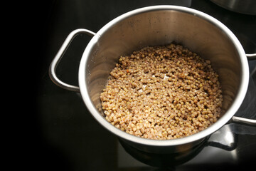 Cooking buckwheat in a steel pot on the black stove top for a healthy gluten free meal, rich source of protein, dietary fiber, four B vitamins and minerals, copy space, selected focus