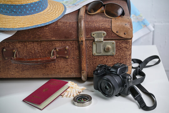 Old brown vintage suitcase with straw hat, photo camera, sunglasses, passport and a map, travel and summer vacation concept, copy space, selected focus