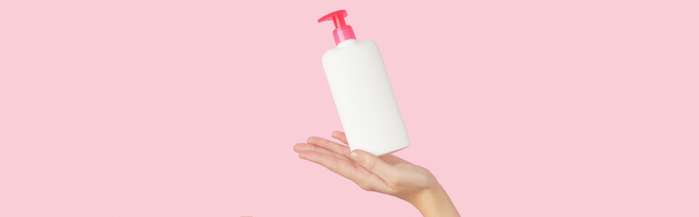 Womans hand holding white bottle on pastel pink background