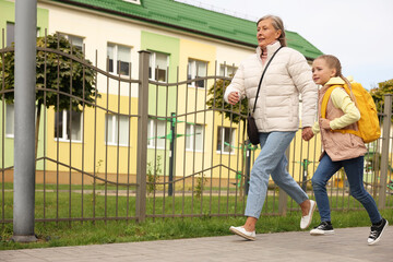 Being late for school. Senior woman and her granddaughter with backpack running outdoors, low angle...