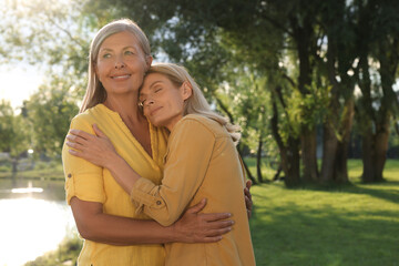 Fototapeta premium Family portrait of happy mother and daughter hugging in park on sunny day. Space for text