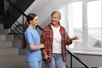 Young healthcare worker assisting senior woman on stairs indoors