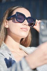 Stylish young woman takes a selfie wearing sunglasses on a sunny day.