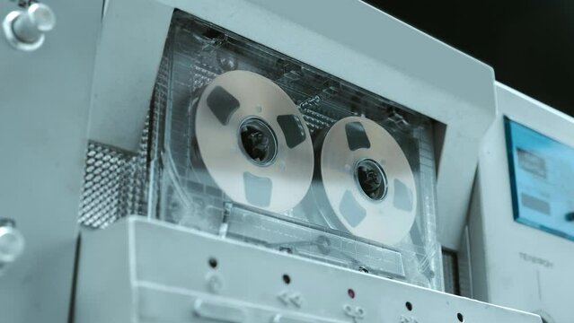 A cassette with gold reels plays music in a Hi-Fi recorder from 80s of silver  color. Closeup. Shot in motion