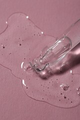Dripping cosmetic serum from pipette onto pink background, macro view
